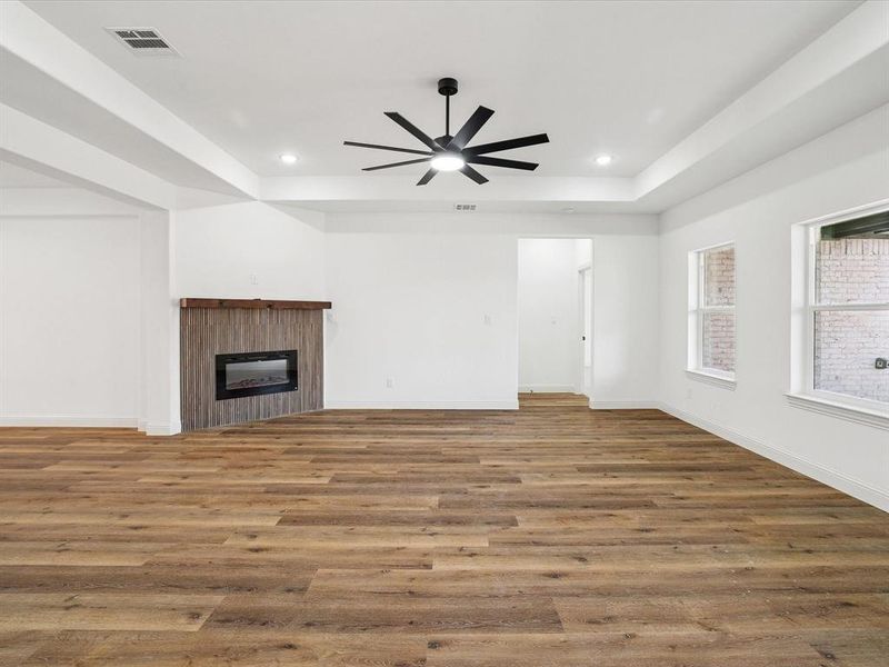Unfurnished living room with a tray ceiling, light wood-style flooring, a glass covered fireplace, ceiling fan, and recessed lighting