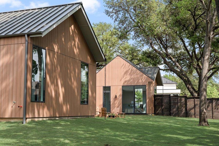 Board and batten siding in natural tones complements the wood-stained fence and mature trees, creating a warm and inviting exterior.