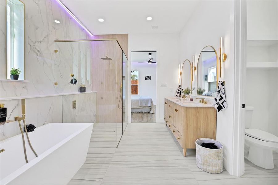 Bathroom featuring a freestanding bath, vanity, a marble finish shower, toilet, and recessed lighting