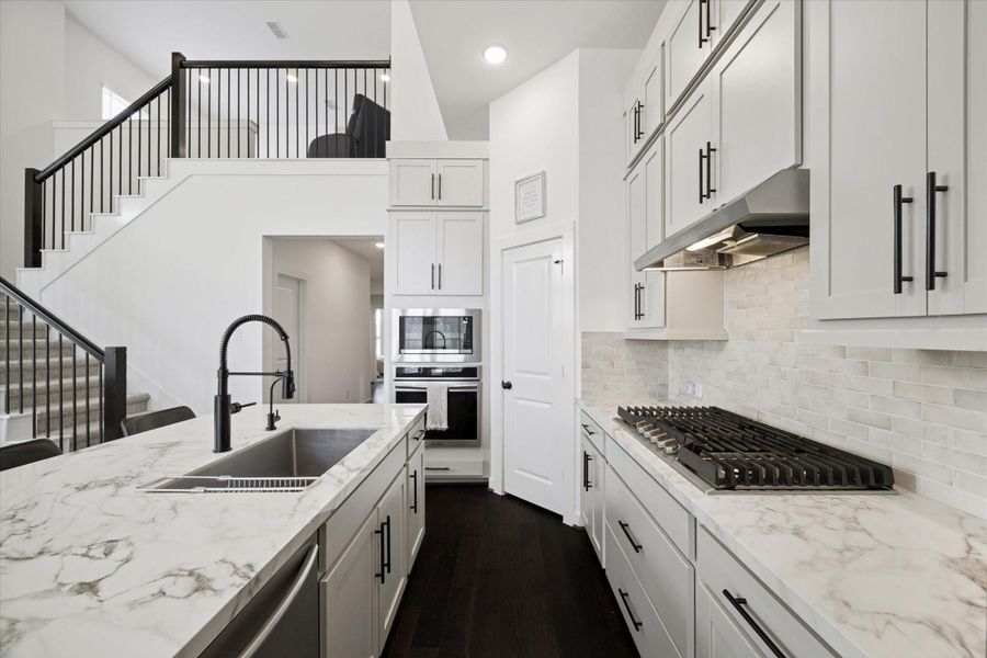 A CLOSE-UP OF THE KITCHEN WORKSPACE HIGHLIGHTS THE GAS COOKTOP, SUBWAY TILE BACKSPLASH, AND BUILT-IN WALL OVEN AND MICROWAVE.