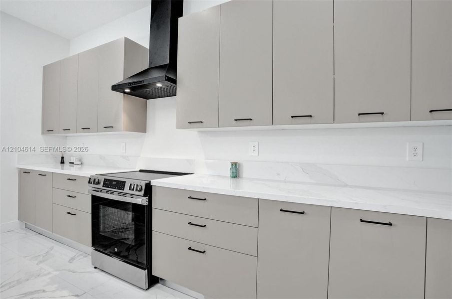Modern kitchen featuring light gray cabinetry, white countertops, black cabinet hardware, a stainless steel range, and a black range hood
