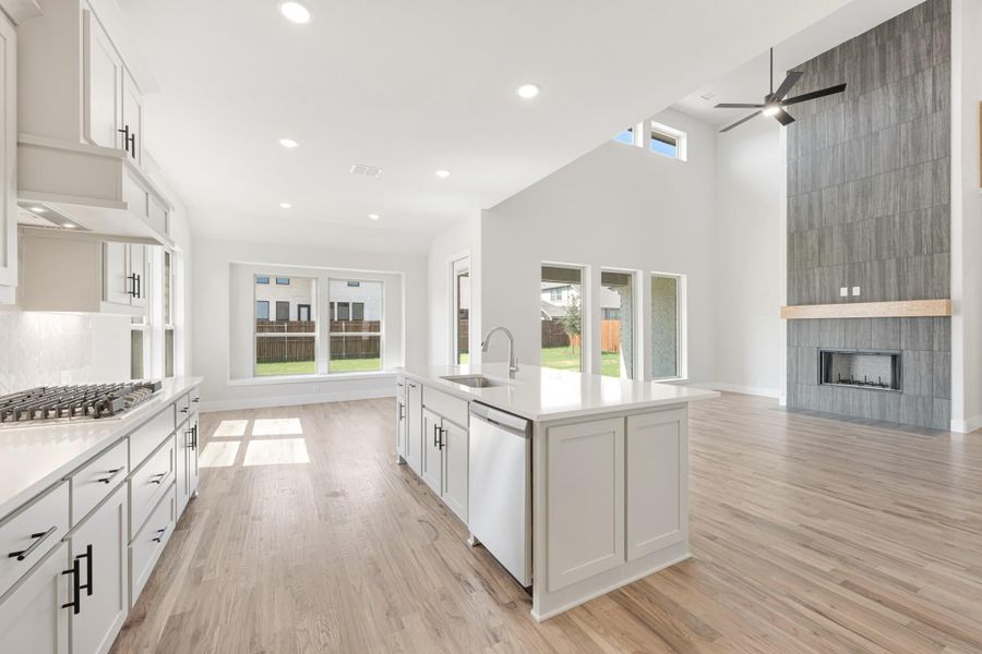 Open kitchen with white cabinets, center island, and light wood floors flowing into living area with tile fireplace