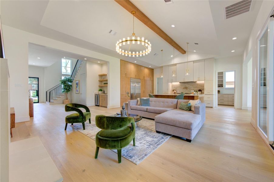 The spacious living room flows effortlessly into the chef’s kitchen, creating a warm and inviting gathering space designed for both everyday living and elegant entertaining. Soaring ceilings with exposed wood beams, designer lighting, and expansive sliding glass doors enhance the open-concept design while filling the space with natural light. Anchored by a stylish fireplace and thoughtfully curated finishes, this seamless connection between living and culinary spaces allows family and guests to gather comfo