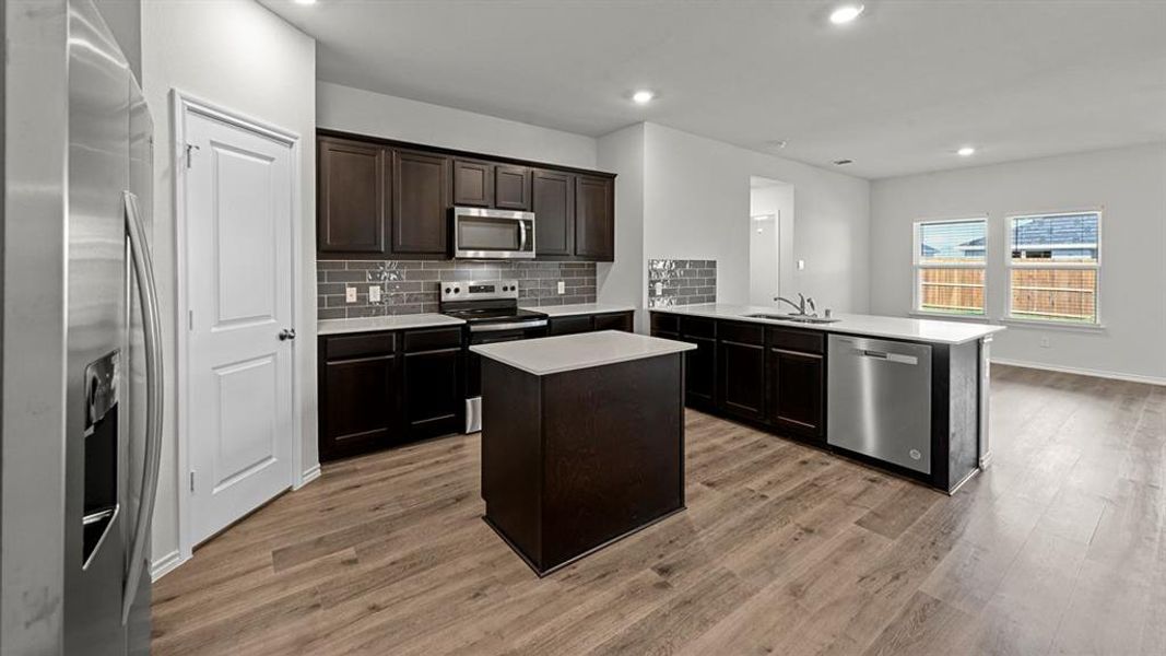 Kitchen with stainless steel appliances, a kitchen island, dark wood finish cabinets, tasteful backsplash, and recessed lighting