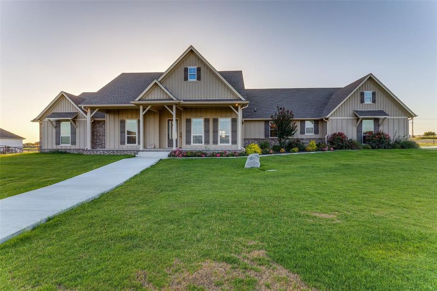 View of front of home with a lawn, a shingled roof, a porch, board and batten siding, and stone siding