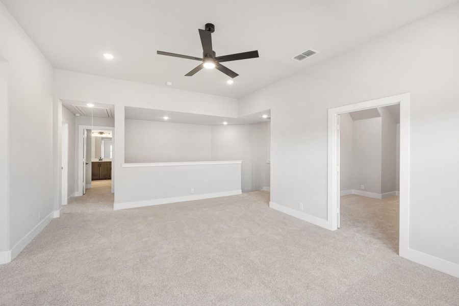 Empty master bedroom with carpet, black ceiling fan, built-in shelving, and walk-in closet doorway Empty master bedroom with carpet, black ceiling fan, built-in shelving, and walk-in closet doorway