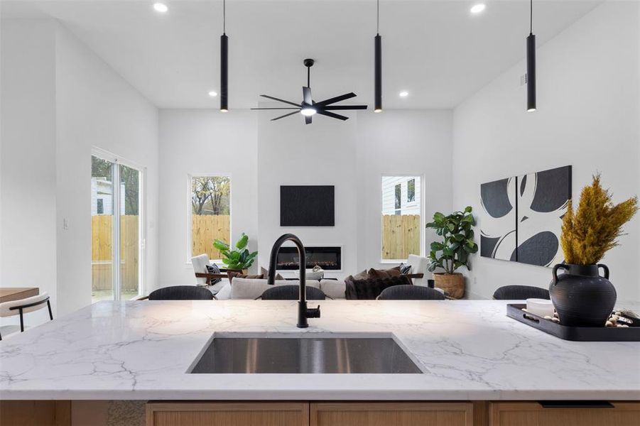Kitchen with light stone countertops, a glass covered fireplace, open floor plan, recessed lighting, and light brown cabinets