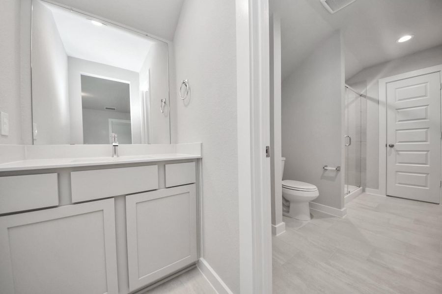 Experience convenience in the secondary bathroom, designed for Jack and Jill arrangements, now with a separate vanity area. This well-appointed space showcases stylish tile flooring, a bath/shower combo with an elegant tile surround, and light-stained wood cabinets. The beautiful light countertop adds a touch of sophistication, combining functionality and aesthetics seamlessly. Sample photo of completed home with similar floor plan. Actual colors and selections may vary.