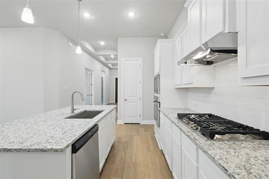 Kitchen with light wood-type flooring, light stone counters, pendant lighting, appliances with stainless steel finishes, and recessed lighting Kitchen with light wood-type flooring, light stone counters, pendant lighting, appliances with stainless steel finishes, and recessed lighting