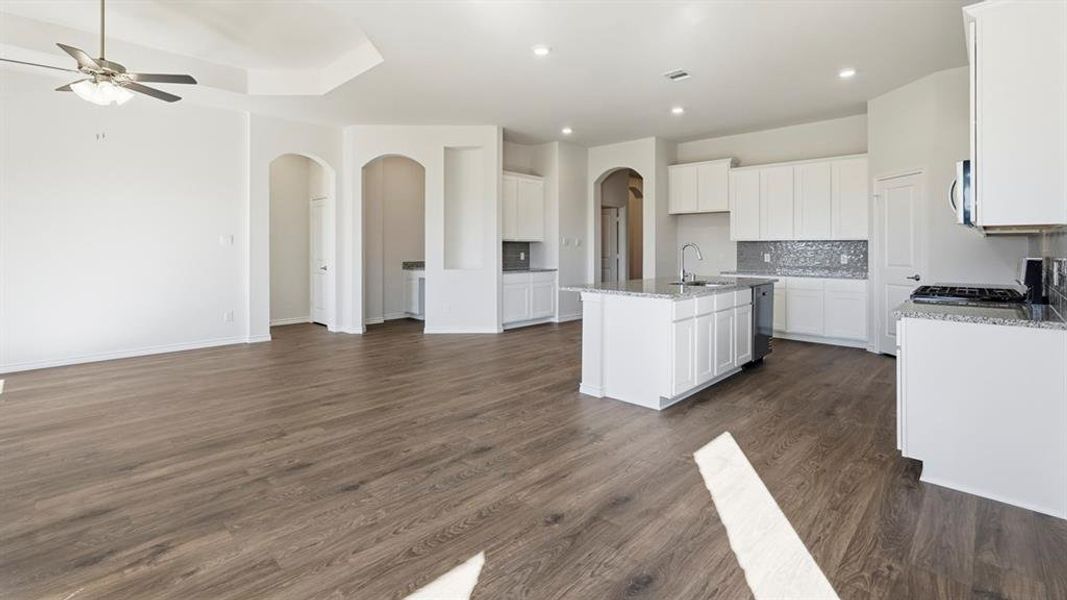 Open concept living area featuring wood-look flooring, a ceiling fan, and a kitchen with white cabinetry, a kitchen island, and recessed lighting Open concept living area featuring wood-look flooring, a ceiling fan, and a kitchen with white cabinetry, a kitchen island, and recessed lighting