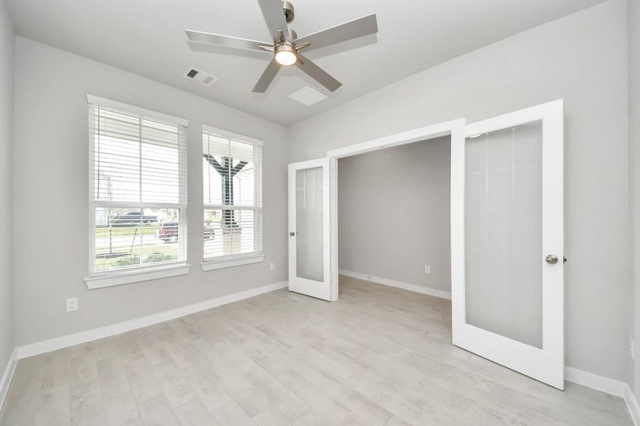 Experience the perfect blend of sophistication and warmth in this home office, boasting elegant wood-look tile flooring and flooded with natural light from expansive windows and French doors.