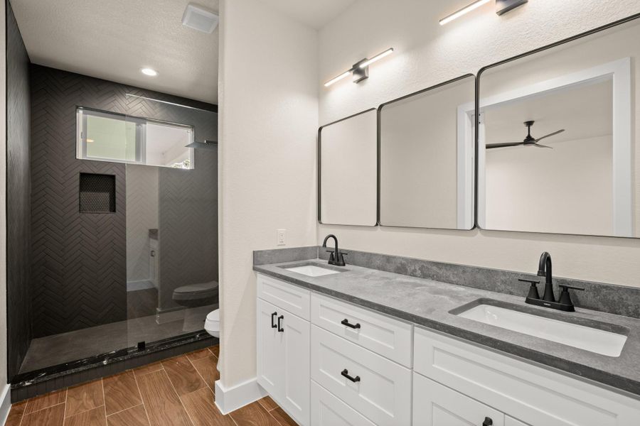 Full bathroom featuring a ceiling fan, double vanity, and tiled shower