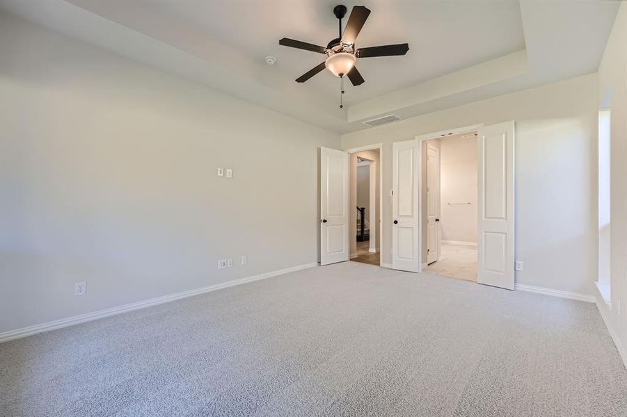 Unfurnished bedroom with light carpet, ensuite bath, a raised ceiling, and ceiling fan