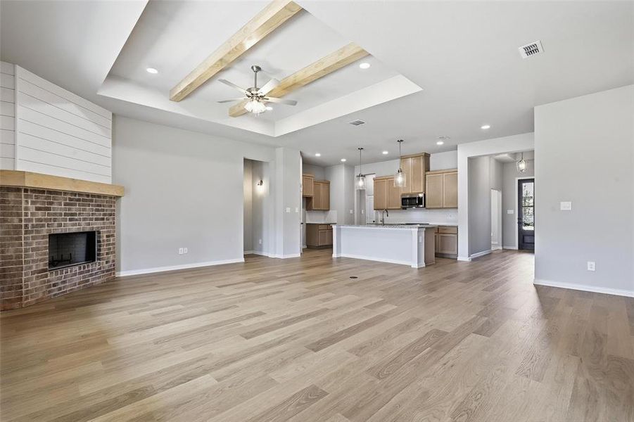 Unfurnished living room with beam ceiling, a ceiling fan, recessed lighting, a fireplace, and light wood finished floors Unfurnished living room with beam ceiling, a ceiling fan, recessed lighting, a fireplace, and light wood finished floors