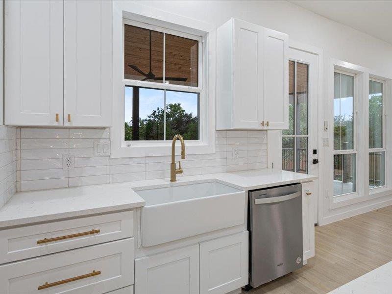 The kitchen features white cabinetry with gold hardware, a white farmhouse sink with a gold faucet, a stainless steel dishwasher, and a white subway tile backsplash