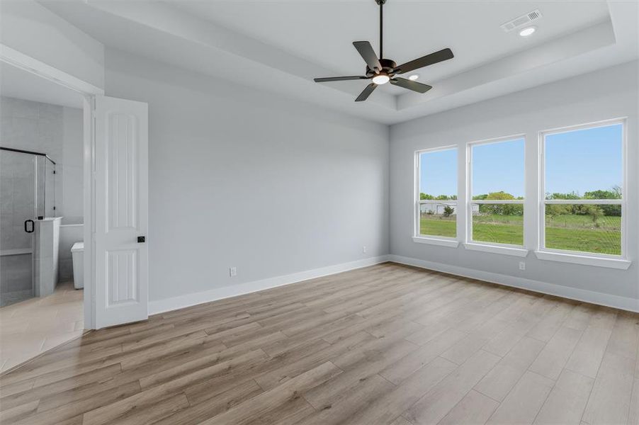 Unfurnished bedroom with a raised ceiling, ceiling fan, and light wood-style flooring