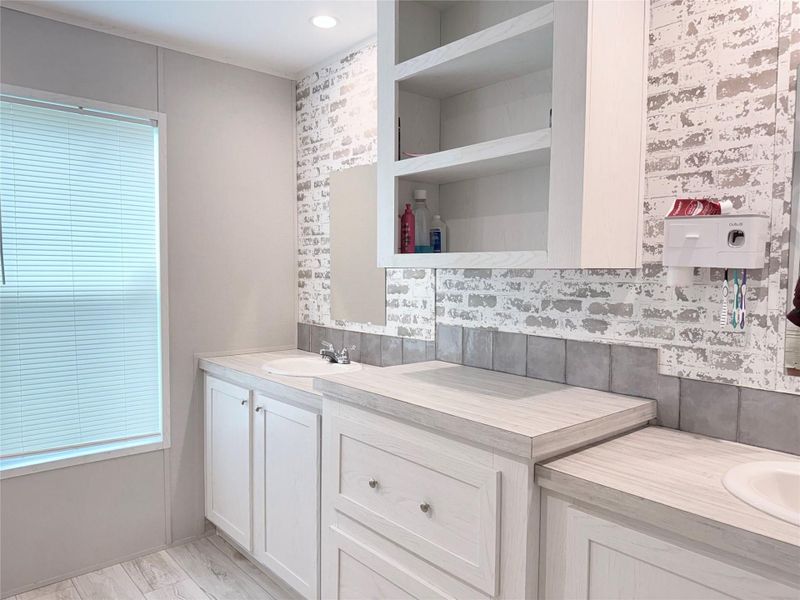 A well-lit bathroom vanity with modern fixtures and ample storage, complemented by unique brick-patterned wall accents.