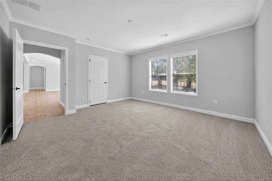 Spare room featuring ornamental molding, arched walkways, and light colored carpet Spare room featuring ornamental molding, arched walkways, and light colored carpet