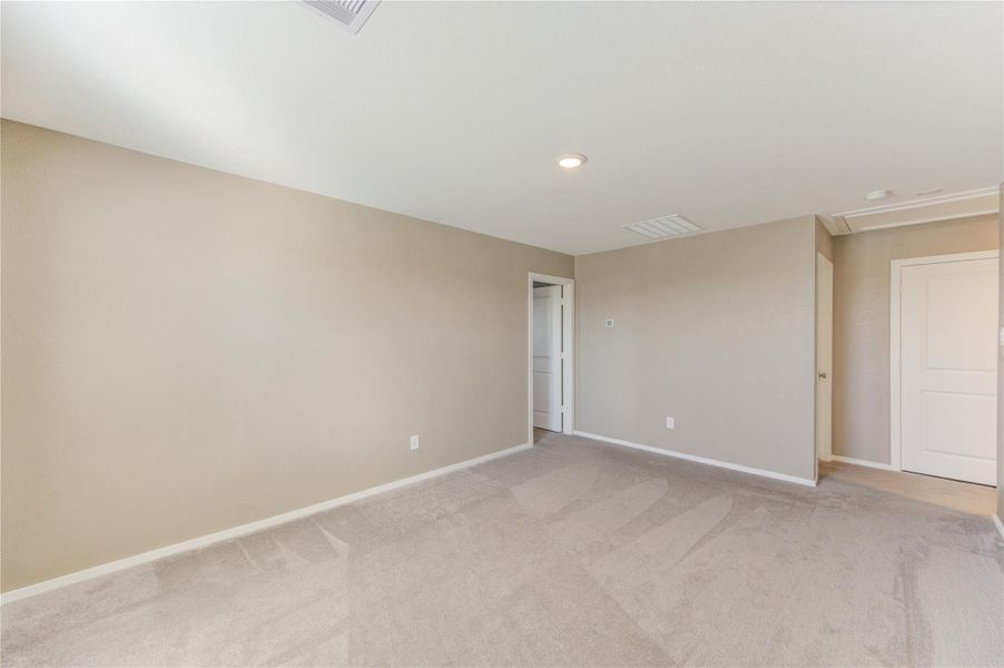 This photo shows a spacious, carpeted room with neutral-colored walls and ceiling. It features recessed lighting and leads to a hallway with white doors, offering a clean and versatile space.