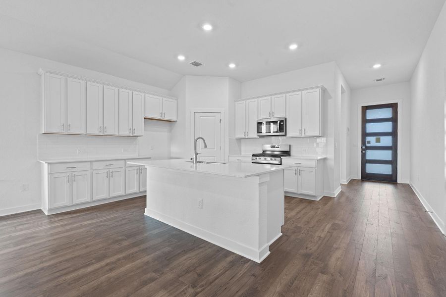 Kitchen with tasteful backsplash, white cabinetry, a kitchen island with sink, appliances with stainless steel finishes, and dark wood-style flooring Kitchen with tasteful backsplash, white cabinetry, a kitchen island with sink, appliances with stainless steel finishes, and dark wood-style flooring