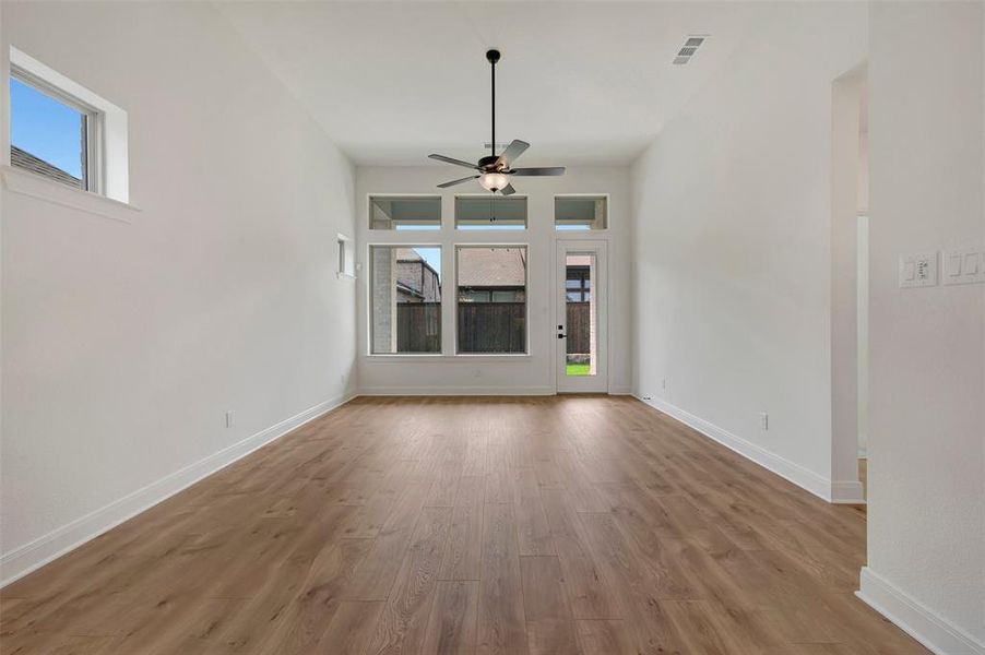 Spacious room featuring wood-finish flooring, high ceilings, and abundant natural light from multiple windows and a glass-paneled door