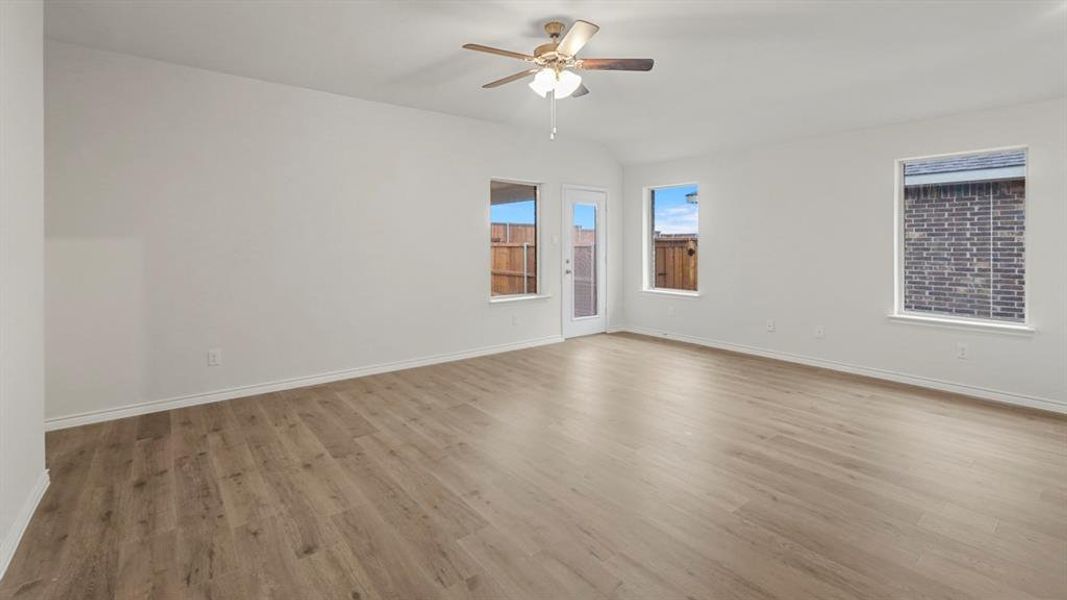 Spacious room featuring wood-finish flooring, white walls, multiple windows, a glass-paned door, and a ceiling fan with integrated lighting