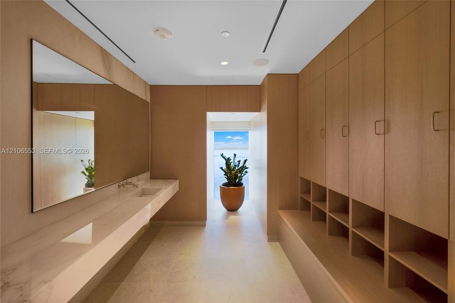 Full-height wood-finish cabinetry with open cubbies, floating stone-surface vanity with an integrated sink, wall-mounted faucet, and a large rectangular mirror