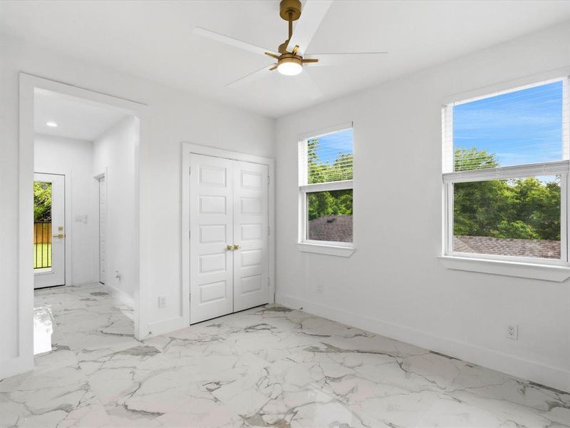 Spacious room featuring white walls, large windows with horizontal blinds, and a contemporary ceiling fan with integrated lighting