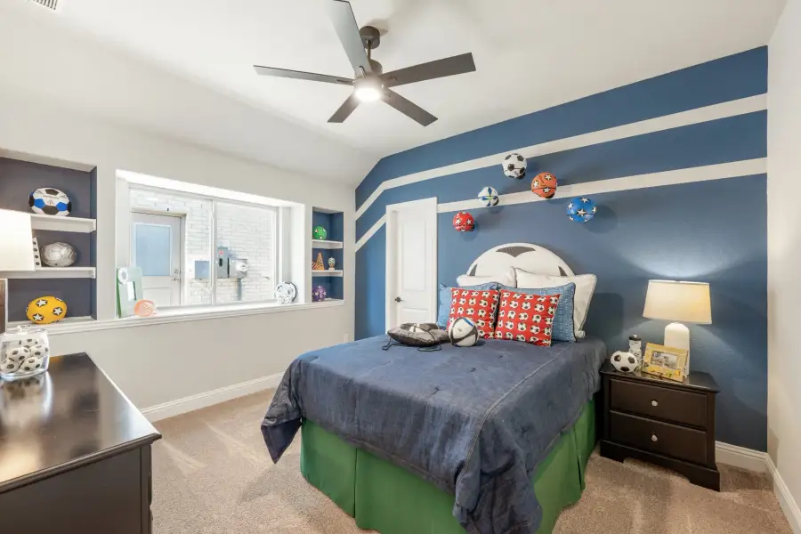 Kids' bedroom with blue accent wall, sports-themed decor, built-in shelves, and ceiling fan