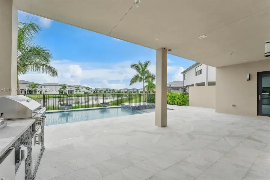 Covered lanai featuring large-format tile flooring, outdoor kitchen with stainless steel grill, in-ground pool with spillover spa, and metal fencing