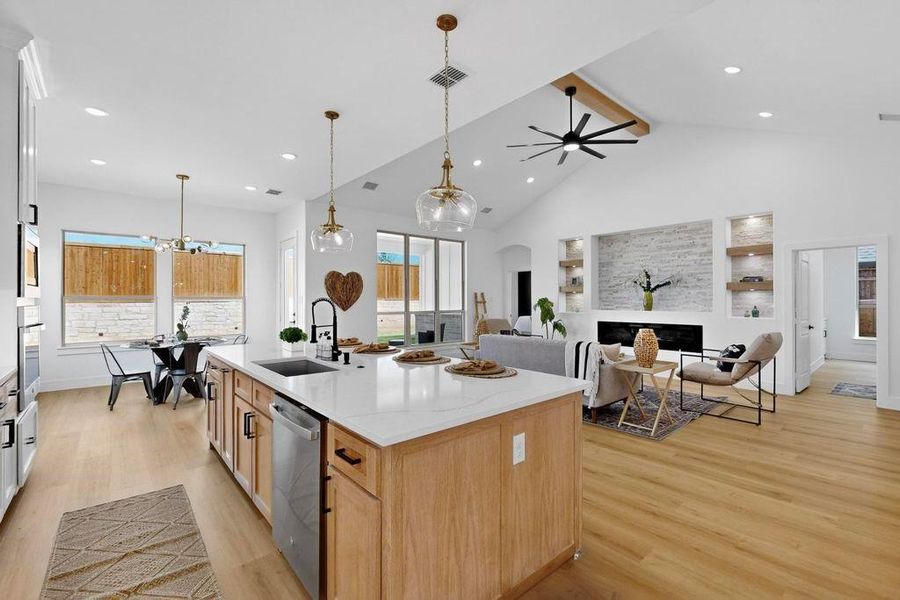 Kitchen featuring beam ceiling, light wood-style flooring, a fireplace, high vaulted ceiling, and light brown cabinets