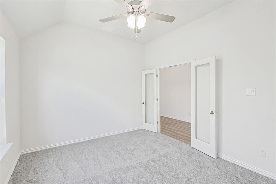 Spare room with ceiling fan, lofted ceiling, and light carpet