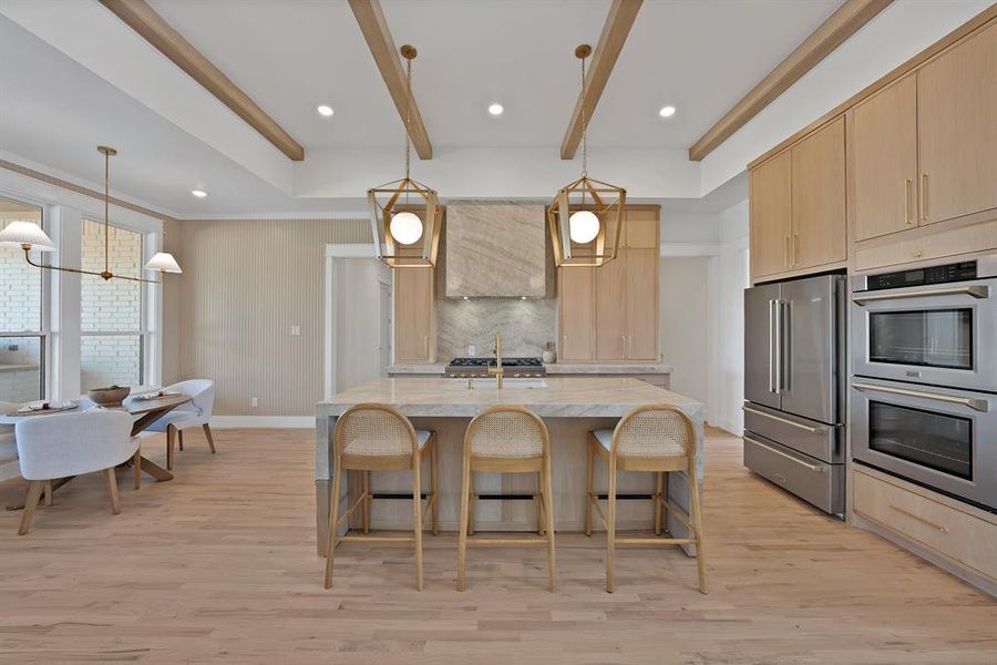Kitchen with light brown cabinets, appliances with stainless steel finishes, a kitchen bar, decorative light fixtures, and beam ceiling