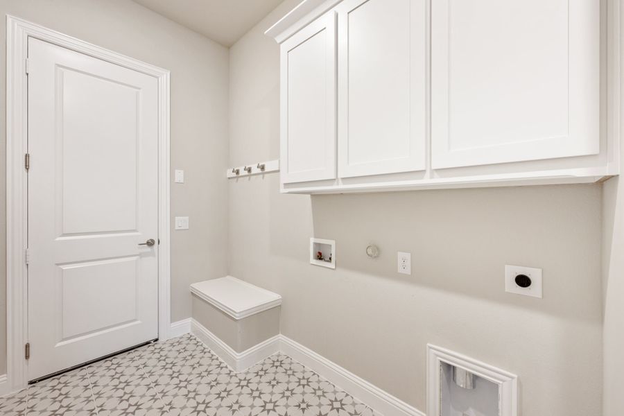 Laundry room with white upper cabinets, wall hooks, washer hookups, and patterned tile floor