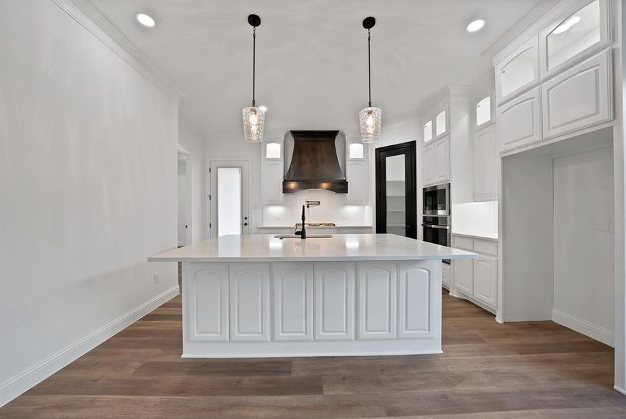 Kitchen featuring white cabinets, glass insert cabinets, decorative light fixtures, an island with sink, and dark wood-type flooring