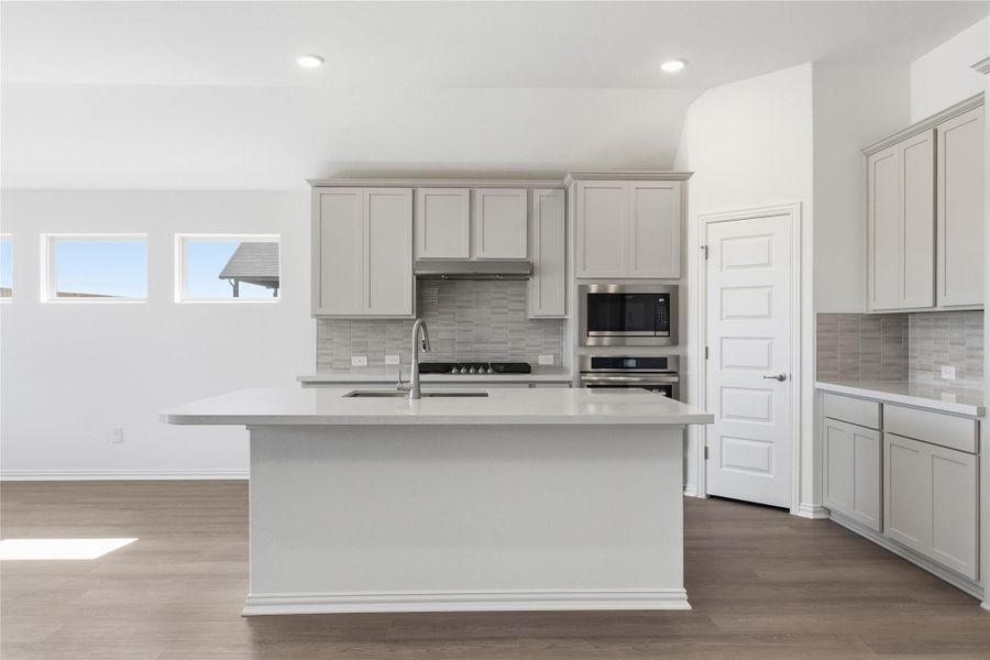 Kitchen with an island with sink, dark wood finished floors, light stone countertops, appliances with stainless steel finishes, and tasteful backsplash