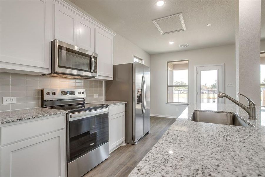 Kitchen featuring stainless steel appliances, decorative backsplash, light stone countertops, white cabinets, and dark wood finished floors