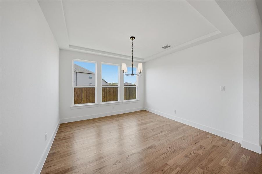 Unfurnished dining area featuring a tray ceiling, light wood finished floors, and a chandelier Unfurnished dining area featuring a tray ceiling, light wood finished floors, and a chandelier