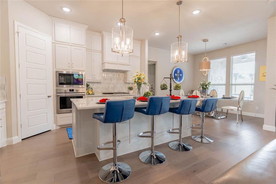 Kitchen with a kitchen island with sink, white cabinetry, a kitchen breakfast bar, hanging light fixtures, and recessed lighting