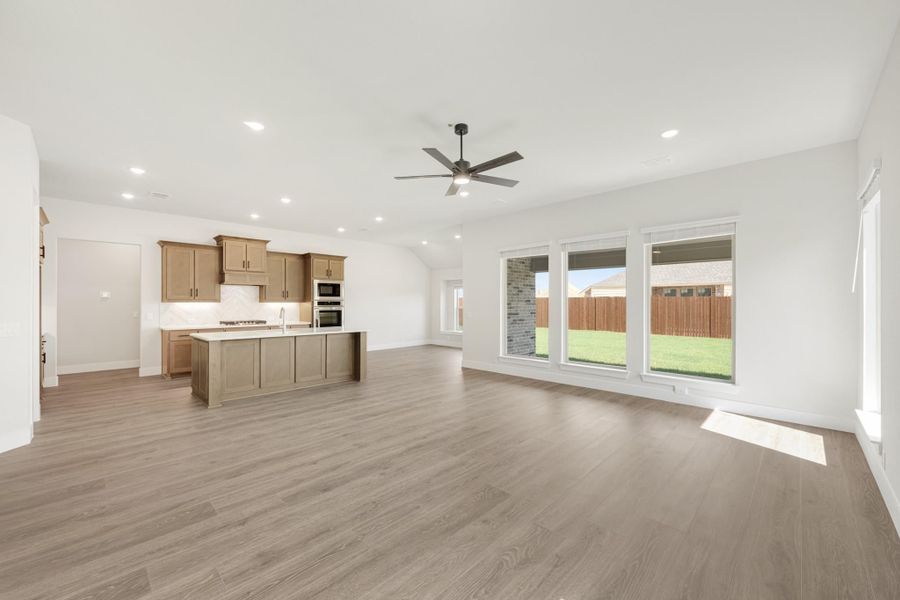 Open living area with hardwood floors and ceiling fan, open to kitchen with island and wood cabinets