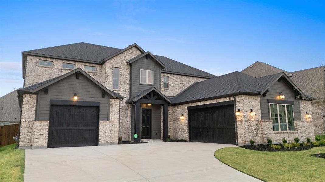 View of front of property featuring a shingled roof, driveway, brick siding, a front lawn, and an attached garage