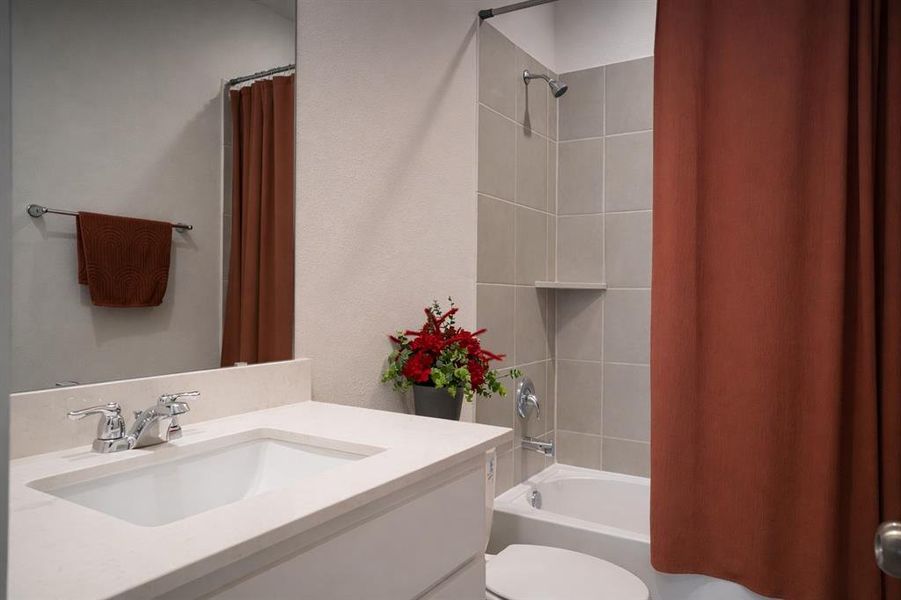 Bathroom featuring a single vanity with an integrated sink and light-toned countertop, a large wall-mounted mirror, and a shower-over-tub combination with light gray wall tiling and a built-in shelf
