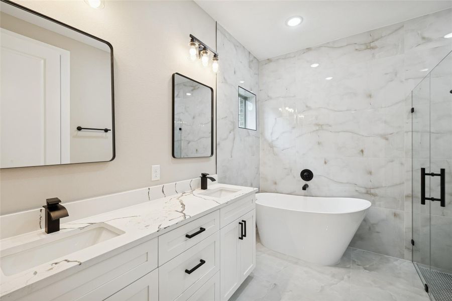 Experience luxury in the primary bath featuring elegant marble tiles, a sleek double vanity, a chic freestanding tub, and a modern glass-enclosed shower.