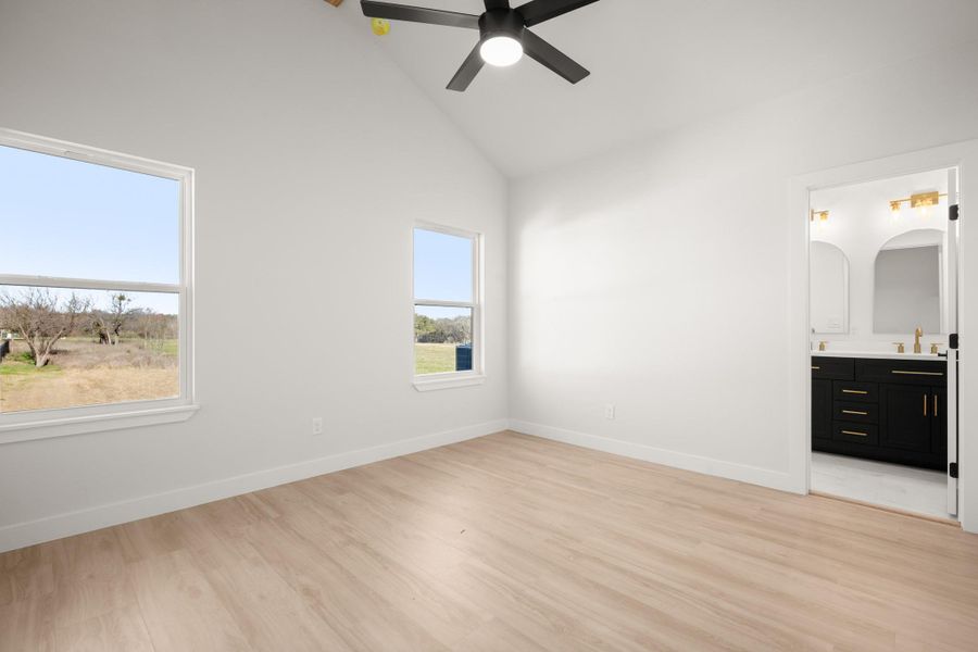 Unfurnished bedroom featuring lofted ceiling, light wood-style flooring, ensuite bath, and ceiling fan