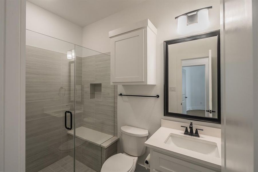 The bathroom features a glass-enclosed shower with a built-in bench, a vanity with a white countertop and sink, and a framed mirror with an overhead light fixture
