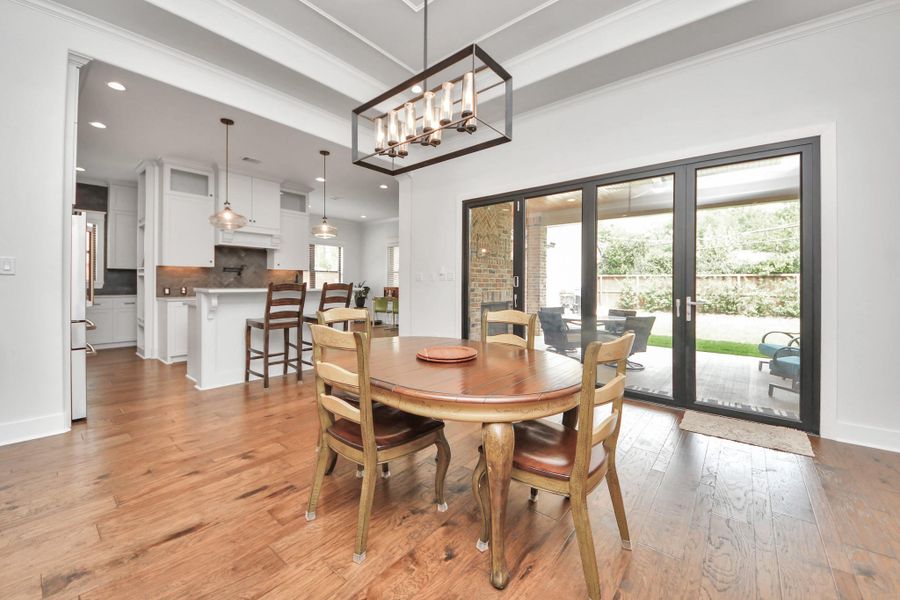 This photo features a bright, open-concept dining area with hardwood floors and a stylish light fixture. It connects to a modern kitchen with an island and bar seating. Large sliding glass doors lead to an outdoor patio, offering a seamless indoor-outdoor living experience.