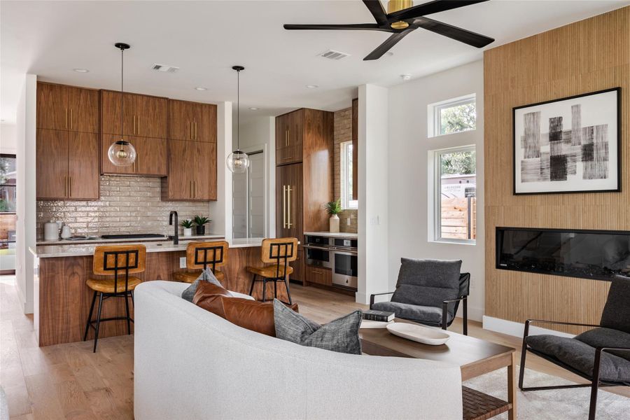 The living room exudes warmth with an electric fireplace and natural wood textures, while a sleek black and gold modern ceiling fan adds an elegant touch to the space.