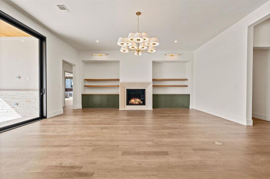 Unfurnished living room with a chandelier, light wood-style flooring, a lit fireplace, and built in features
