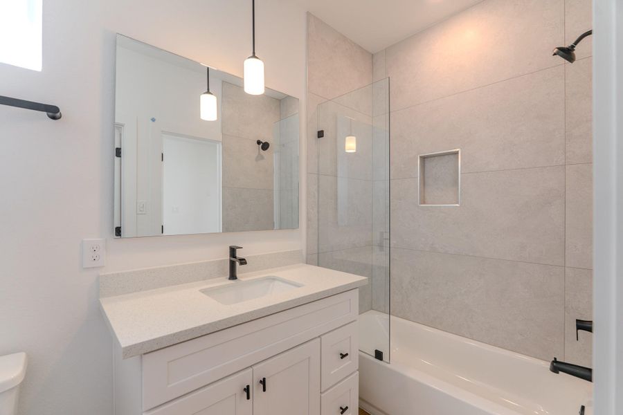 This modern bathroom features a sleek design with a large mirror, stylish pendant lighting, and a glass-enclosed bathtub. The vanity offers ample storage with a contemporary faucet, while the neutral tile creates a clean, elegant look.Photo Disclaimer: Photos are representative of the community and may depict a similar floor plan, model home, or previously completed residence. This modern bathroom features a sleek design with a large mirror, stylish pendant lighting, and a glass-enclosed bathtub. The vanity offers ample storage with a contemporary faucet, while the neutral tile creates a clean, elegant look.Photo Disclaimer: Photos are representative of the community and may depict a similar floor plan, model home, or previously completed residence.