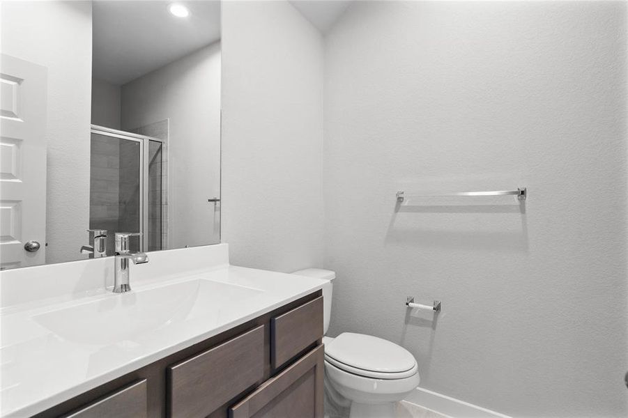 This secondary bath features tile flooring, shower with tile surround, stained wood cabinets, beautiful light countertops, mirror, sleek fixtures and modern finishes.